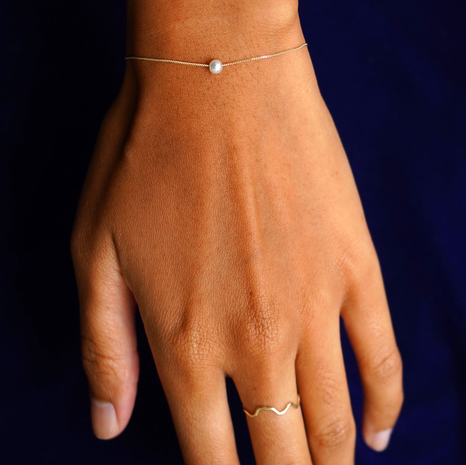 A model wearing a 4mm Pearl Slide Bracelet and a yellow gold Wave Ring