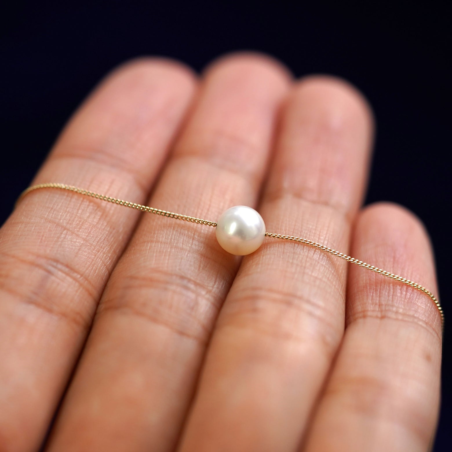 A 6mm pearl slide necklace resting on a model's fingers