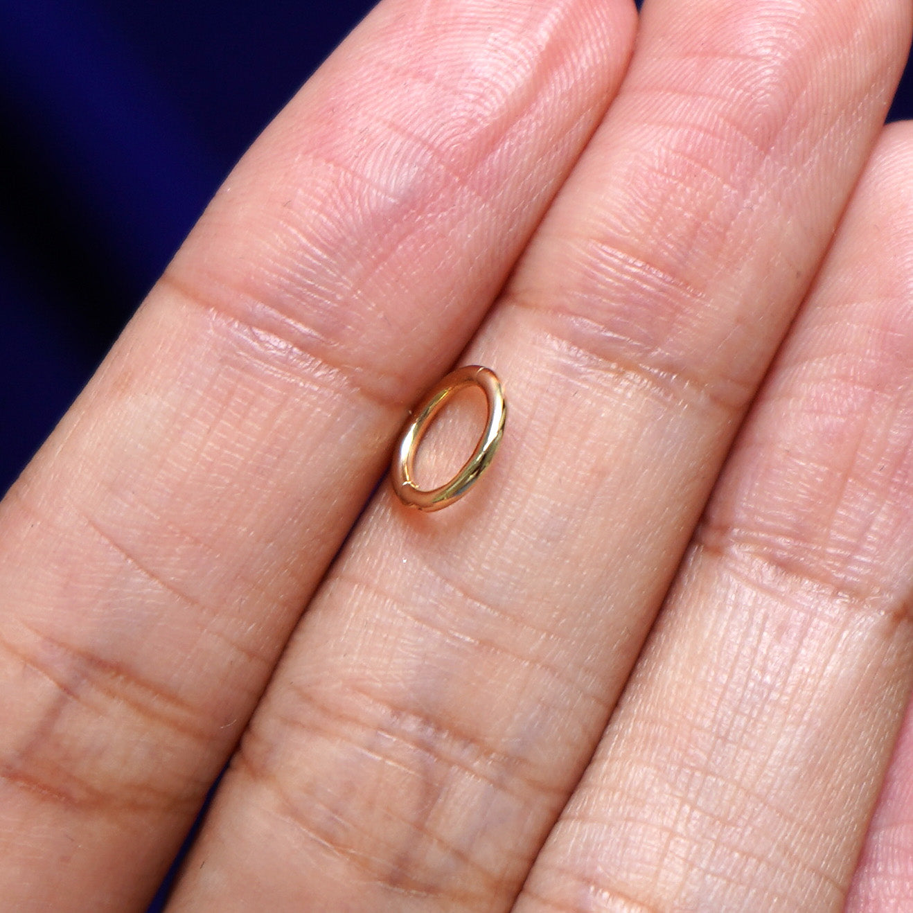 A model holding a Mini Seamless Huggie sideways between two fingers to show the thickness of the hoop