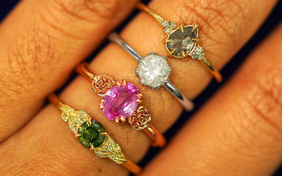 Close up view of a model's hand wearing several different Automic Gold engagement rings stacked on their finger