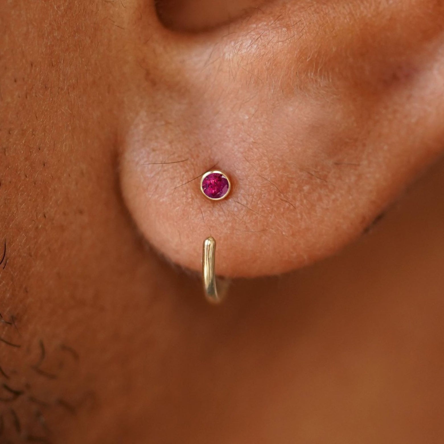 Close up view of a model's ear wearing a 14 karat yellow gold ruby Open Hoop