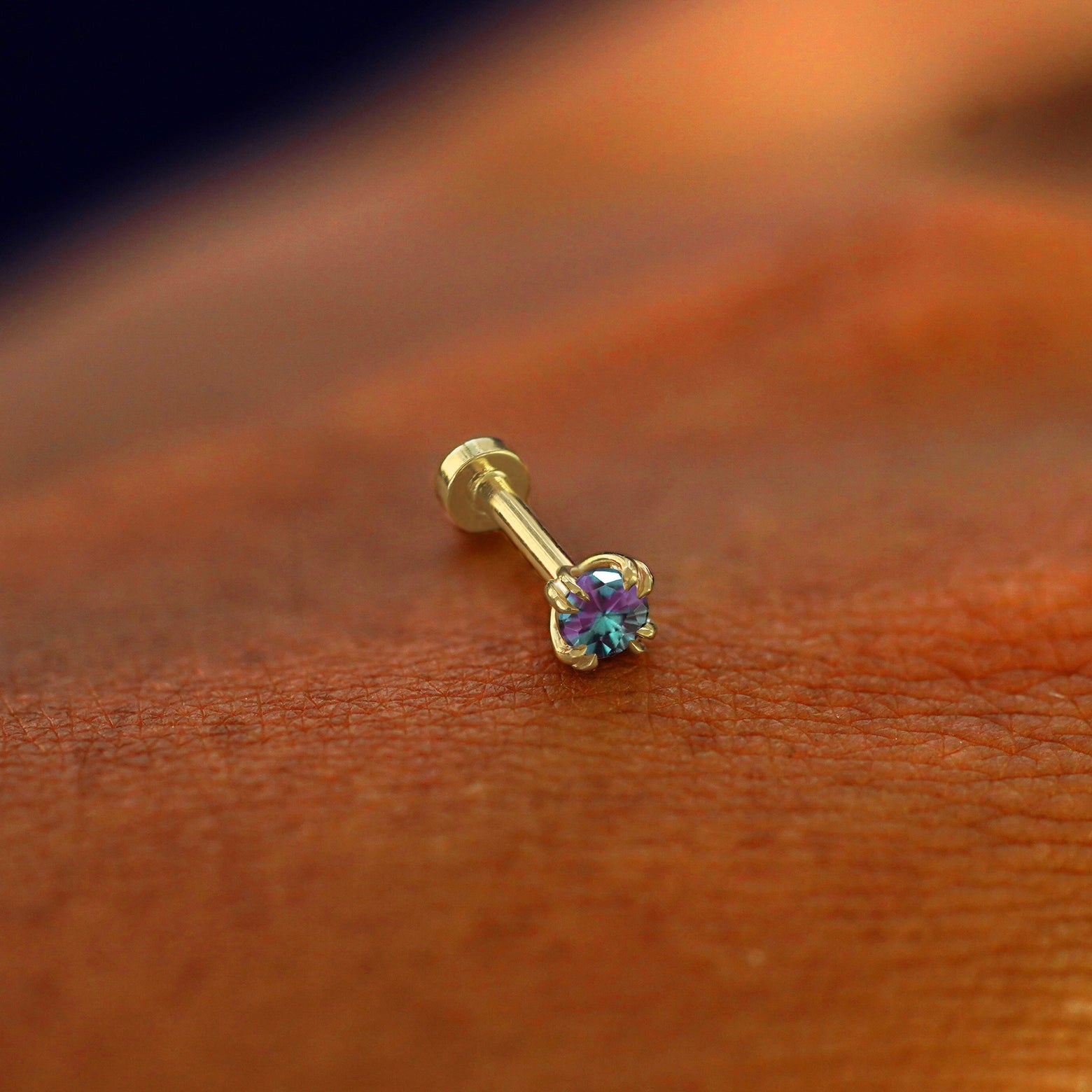 A solid 14k yellow gold Alexandrite Flatback Piercing resting on the back of a model's hand