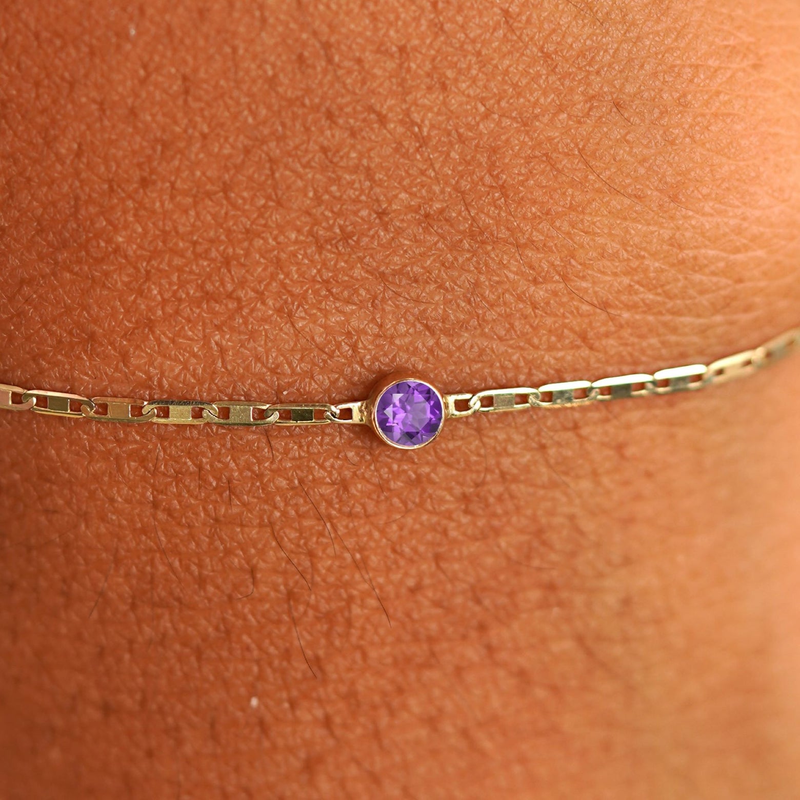 Close up view of a models wrist wearing 14k yellow gold Amethyst Bracelet