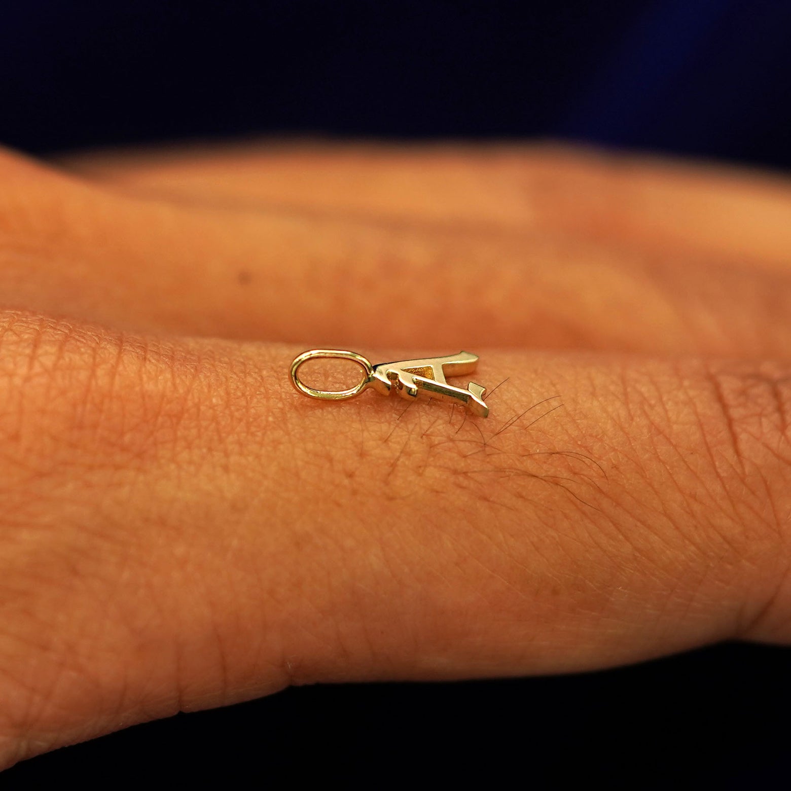 A solid 14k gold Initial Charm for chain in the letter A laying on the back of a model's finger