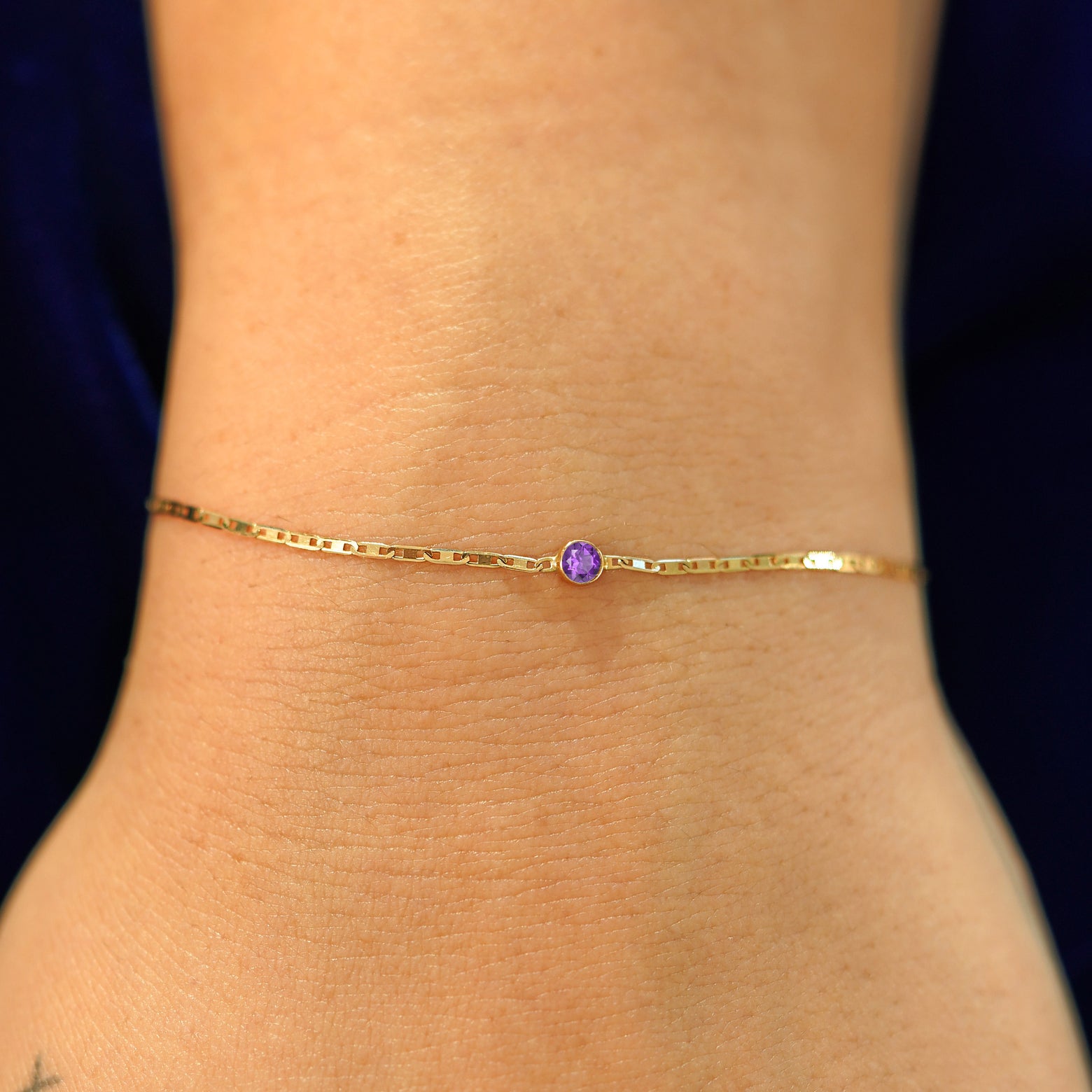 A model's wrist wearing a solid 14k yellow gold Amethyst Bracelet