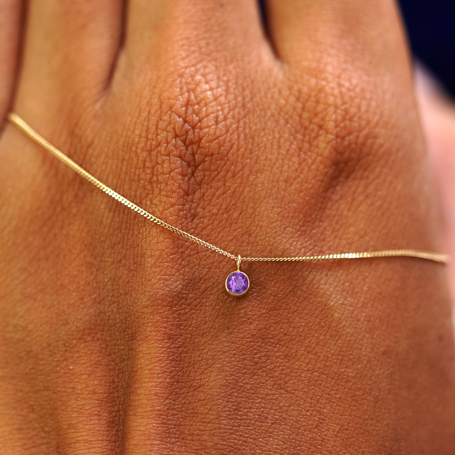 A solid yellow gold Amethyst Necklace draped across the back of a model's hand