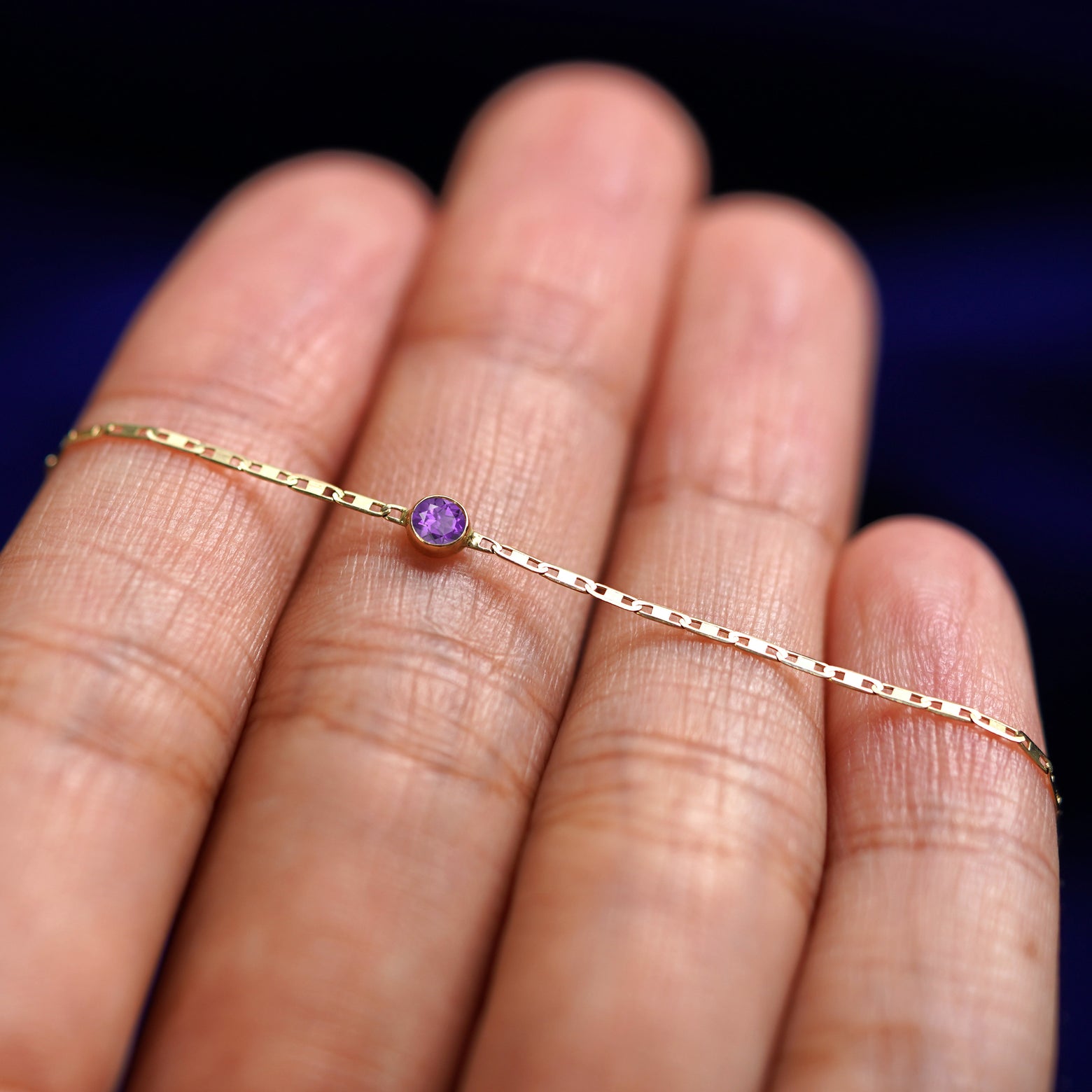 A yellow gold Amethyst Bracelet resting on a model's fingers