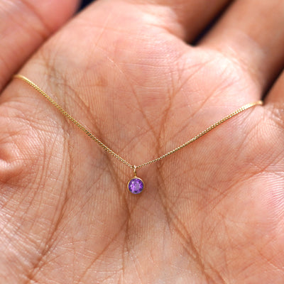 A solid 14k gold Amethyst Necklace resting in a models palm