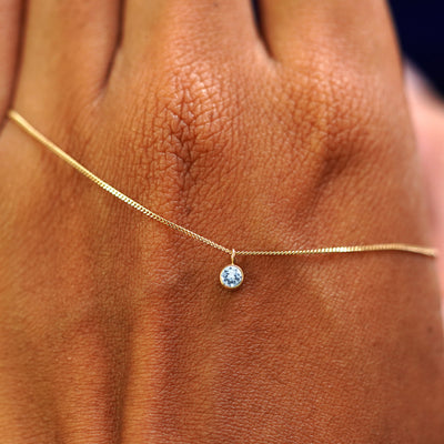 A solid yellow gold Aquamarine Necklace draped across the back of a model's hand