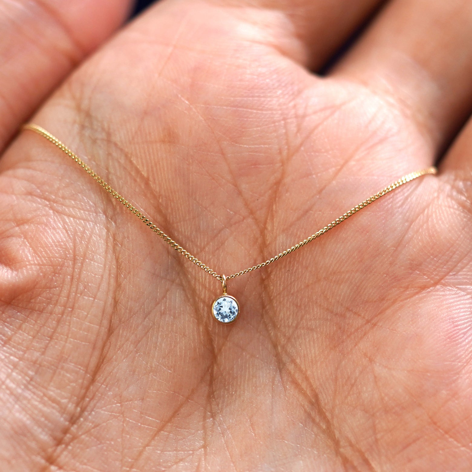 A solid 14k gold Aquamarine Necklace resting in a models palm