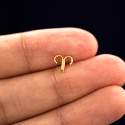A solid 14k yellow gold Aries Horoscope Earring in between a model's fingers