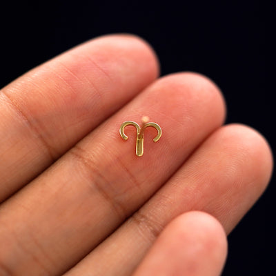 A yellow gold Aries Horoscope Earring laying facedown on a model's fingers to show the underside view