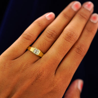 Close up view of a model's hand wearing a yellow gold Asscher Moissanite Signet Ring