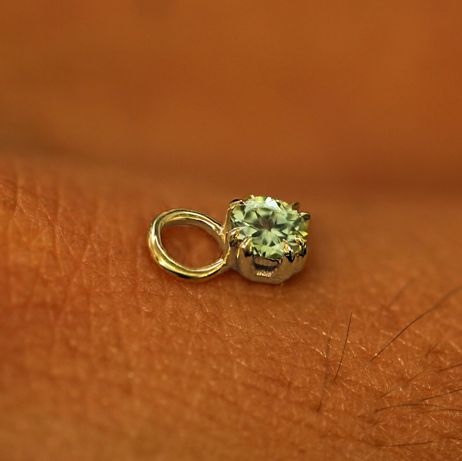 A solid yellow gold Peridot Charm for earring resting on the back of a model's hand