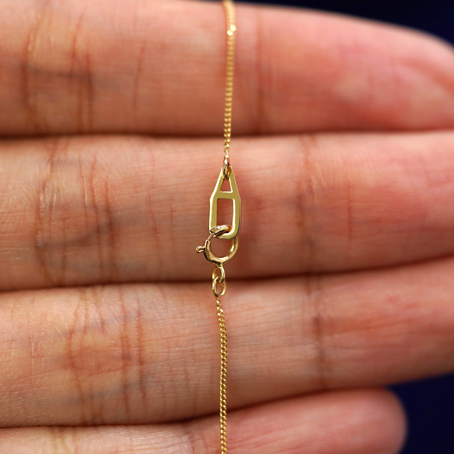A model's hand holding an Automic Gold AU spring ring lock on a yellow gold Essential Chain