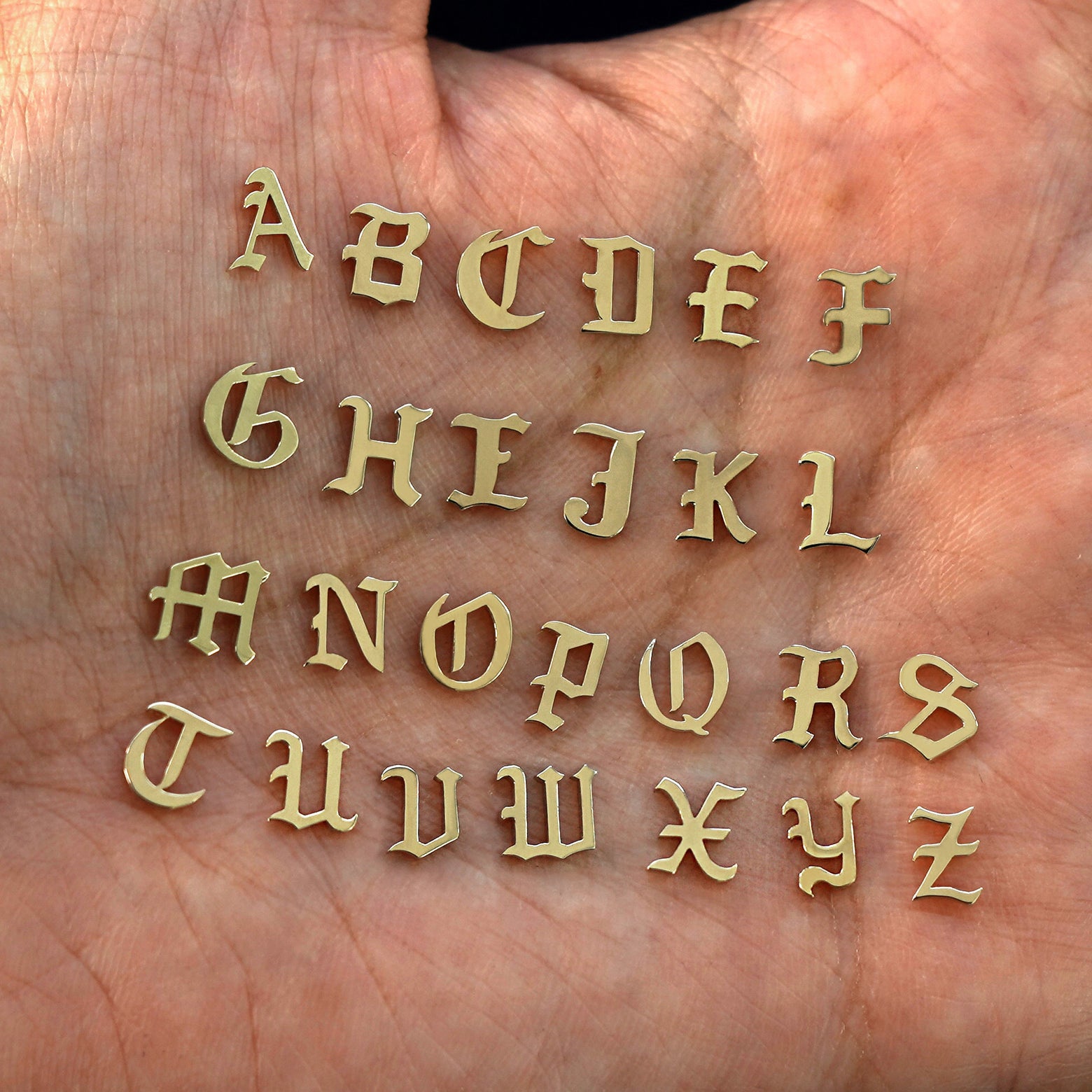 A model's palm holding solid 14k champagne gold versions of all 26 initials in the unique Automic Gold font
