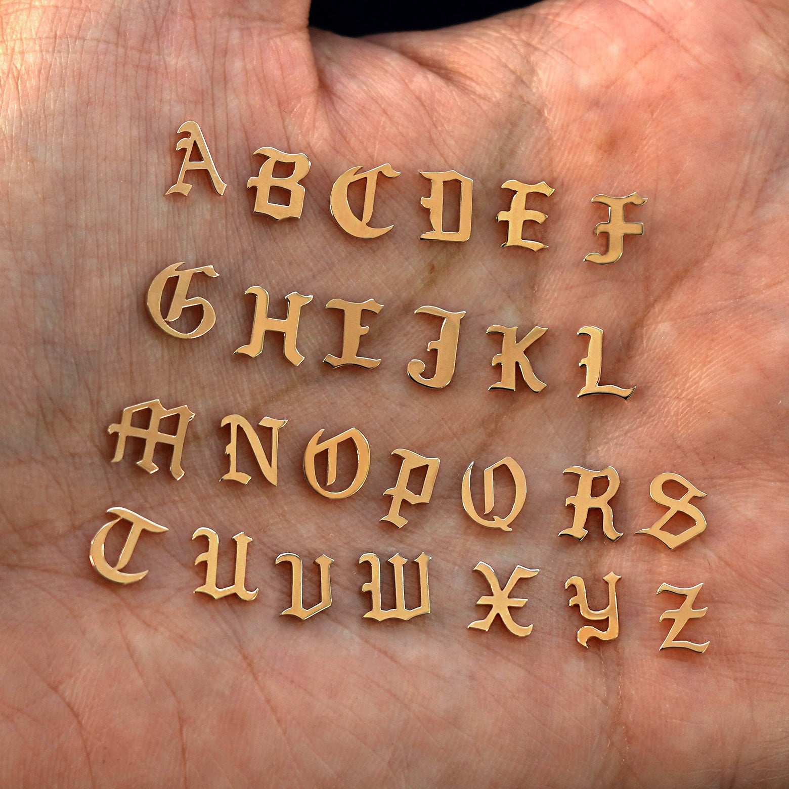 A model's palm holding solid 14k rose gold versions of all 26 initials in the unique Automic Gold font
