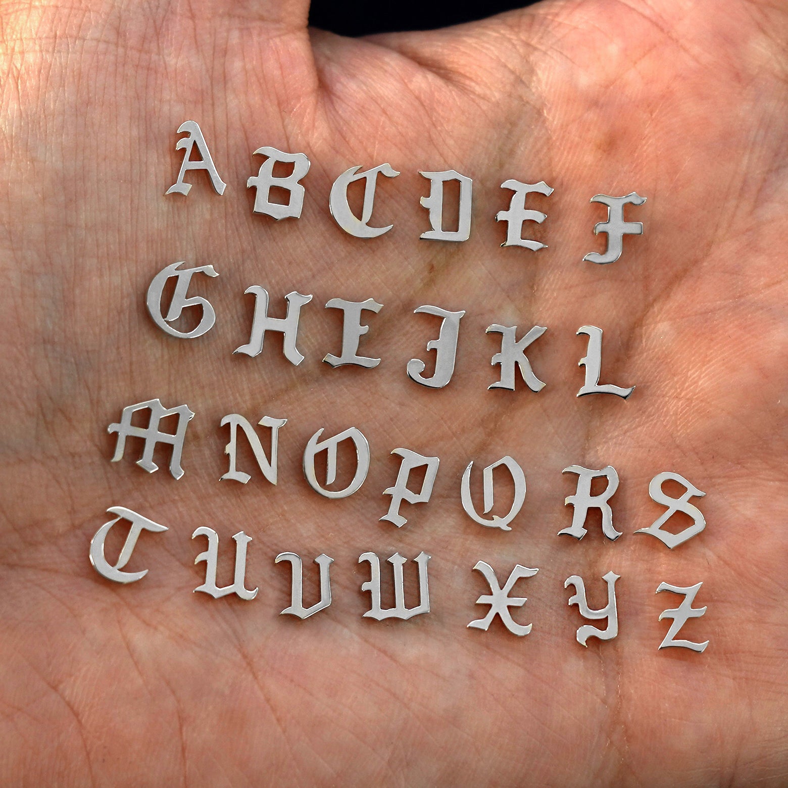 A model's palm holding solid 14k white gold versions of all 26 initials in the unique Automic Gold font