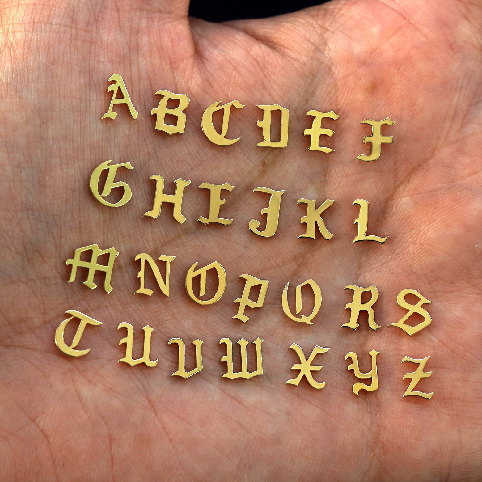 A model's palm holding solid 14k yellow gold versions of all 26 initials in the unique Automic Gold font