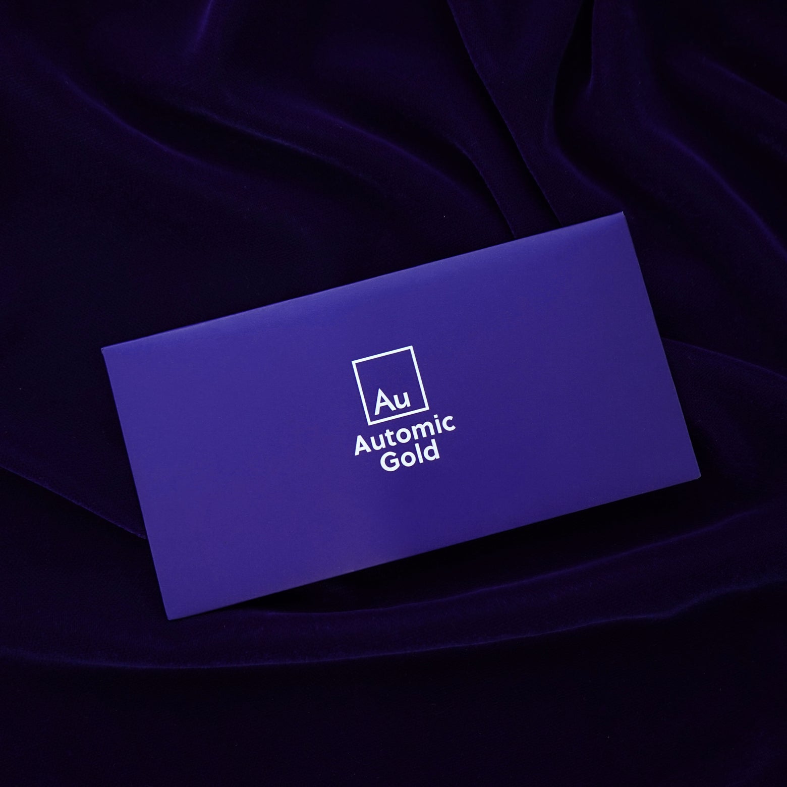 An Automic Gold branded envelope containing a polishing cloth sitting on a dark blue background