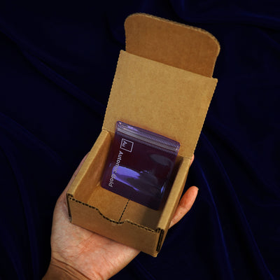 An open Automic Gold Minimal Packaging box held in a model's hand with a jewelry pouch inside