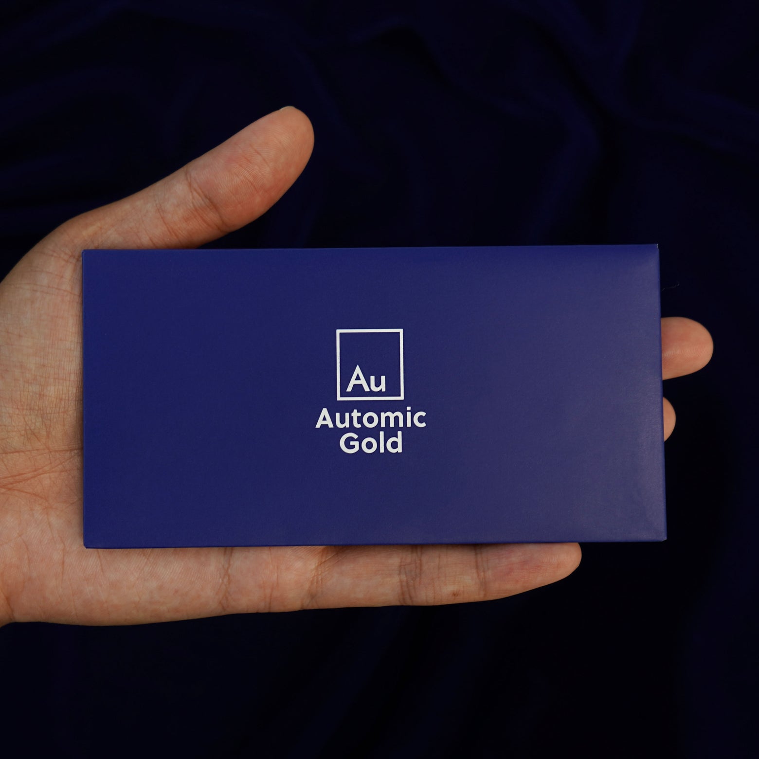 An Automic Gold branded envelope containing a polishing cloth sitting in a model's hand