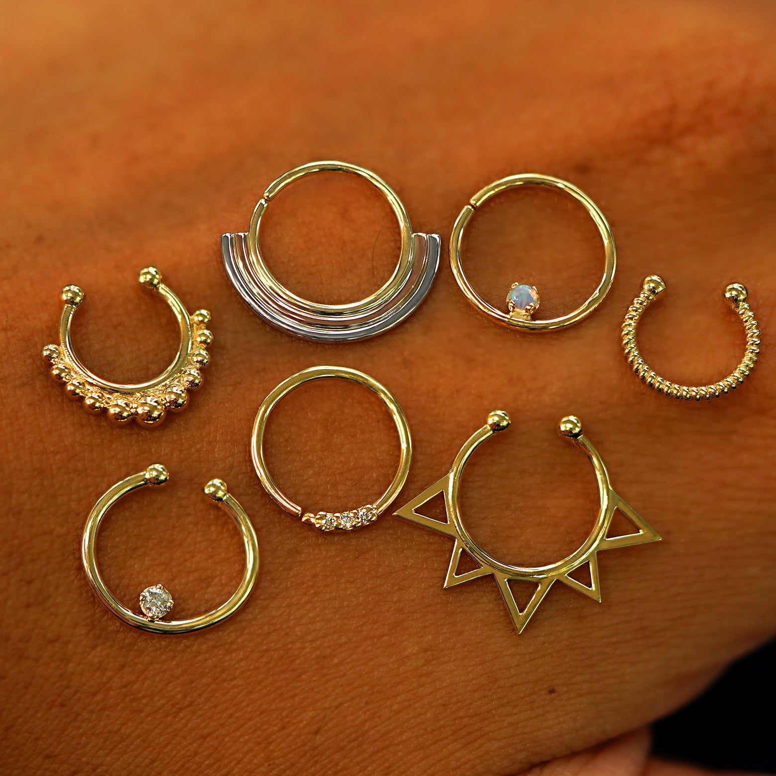 A beaded, rainbow, raised gemstone, rope, raised diamond, triple diamond, and sun septum rings on the back of a model's hand