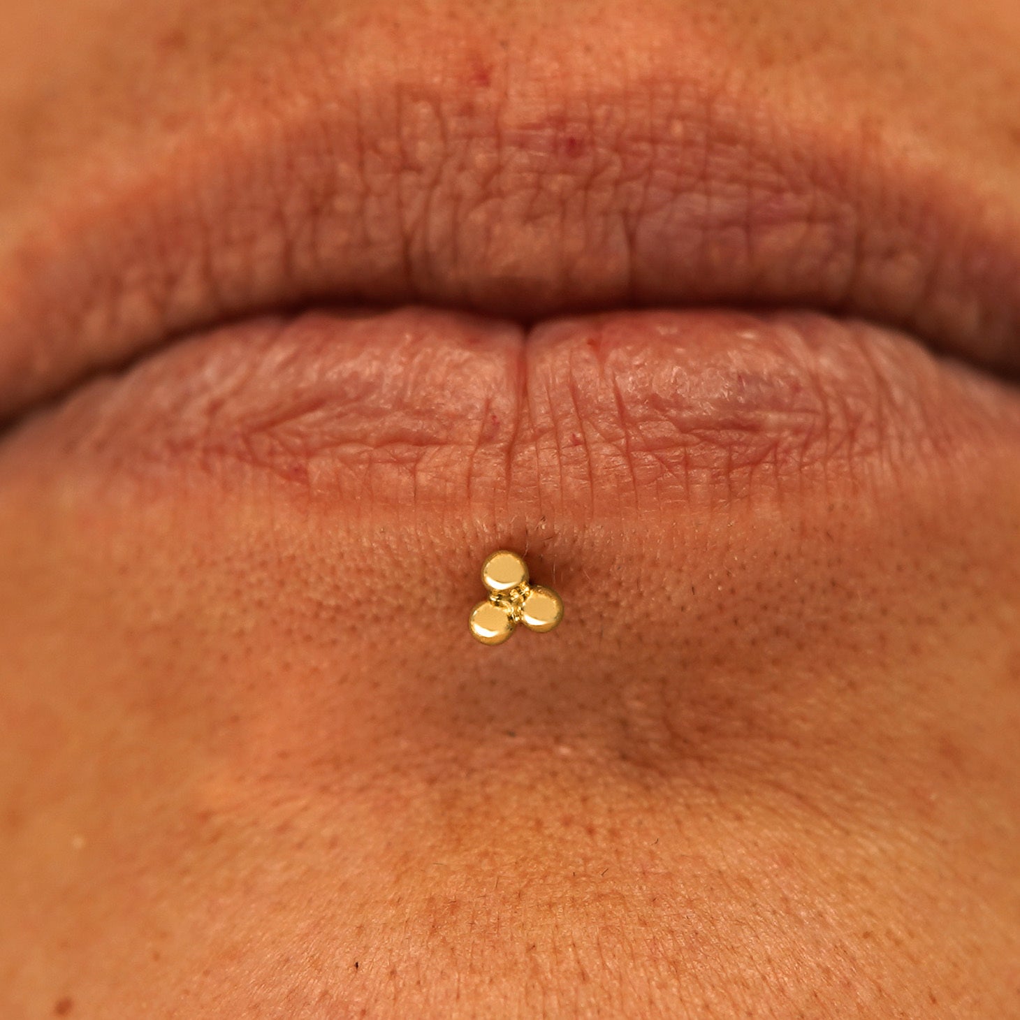 Close up view of a model's mouth wearing a 14k yellow gold Ball Trio Flatback as a labret piercing