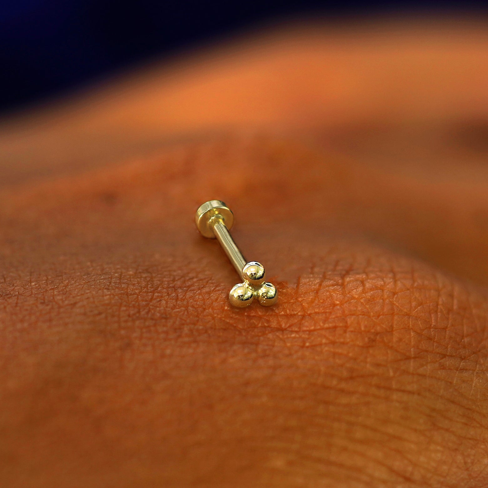 A yellow gold Ball Trio Flatback Piercing laying on the back of a model's hand