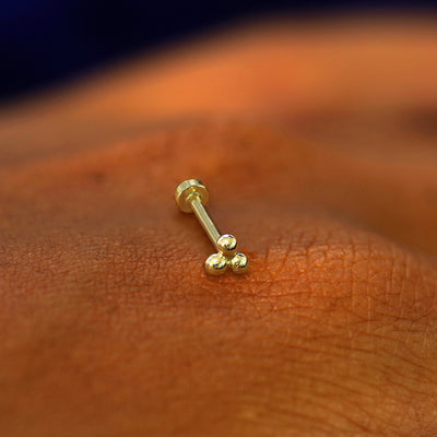 A yellow gold Ball Trio Flatback Piercing laying on the back of a model's hand