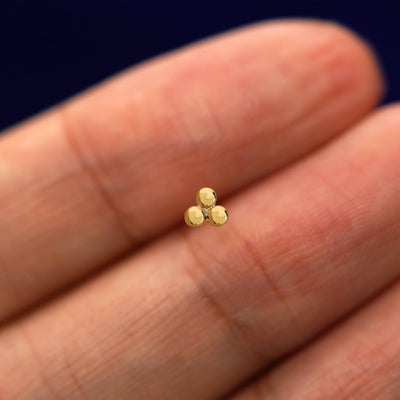 A solid 14k yellow gold Ball Trio Earring in between a model's fingers