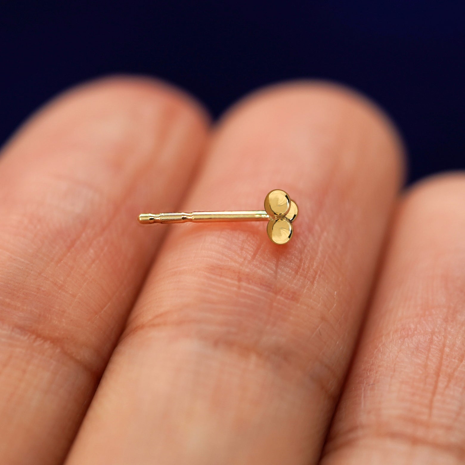 A 14k gold Ball Trio Earring sitting sideways on a model's fingertips to show detail