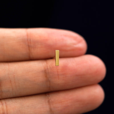 A model holding a single Bar Earring  between their fingers to show the bar