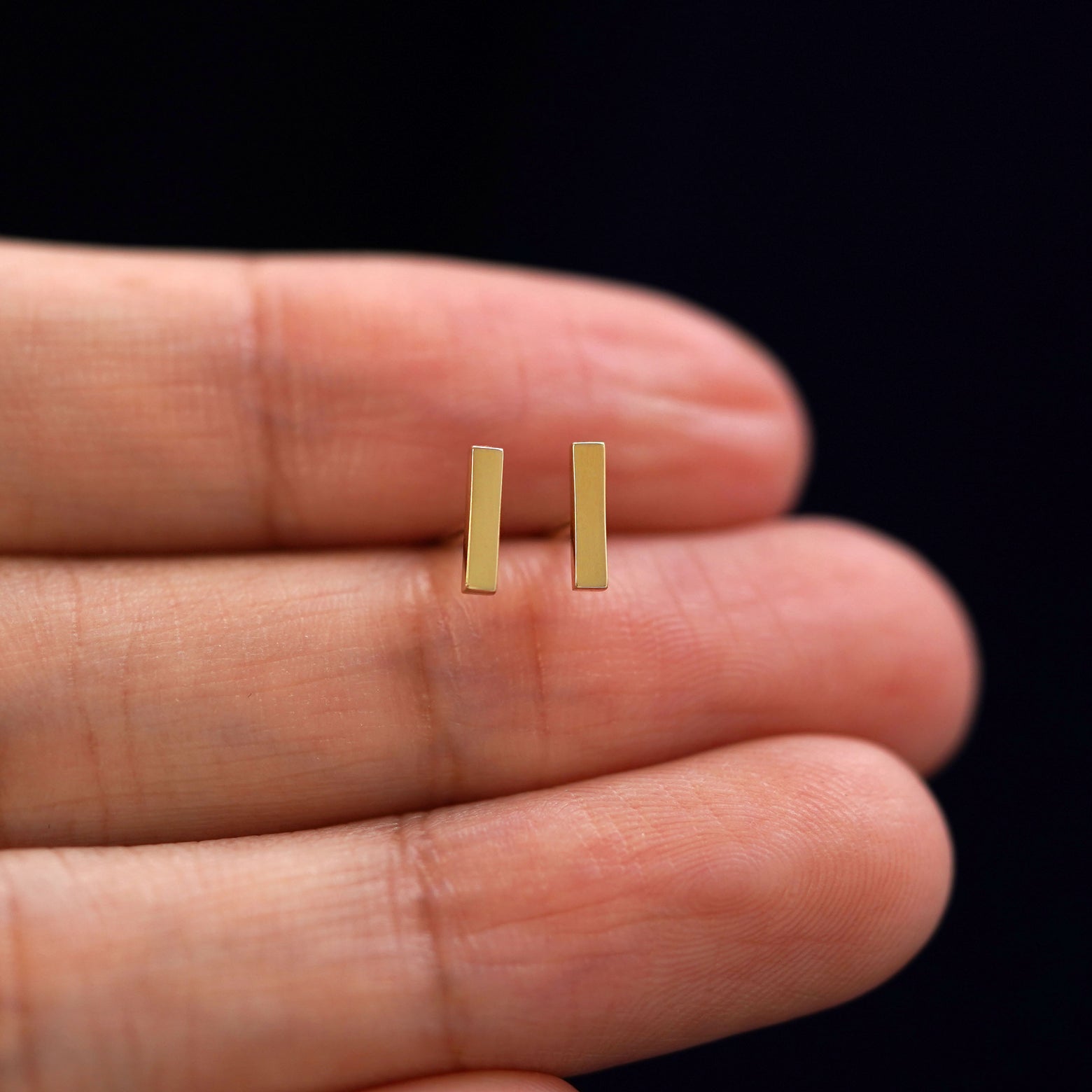 A model holding a pair of solid yellow gold Bar Earrings  between their fingers