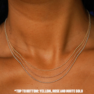 Close up view of a model's neck wearing a three versions of the Bead Necklace in yellow, white, and rose gold