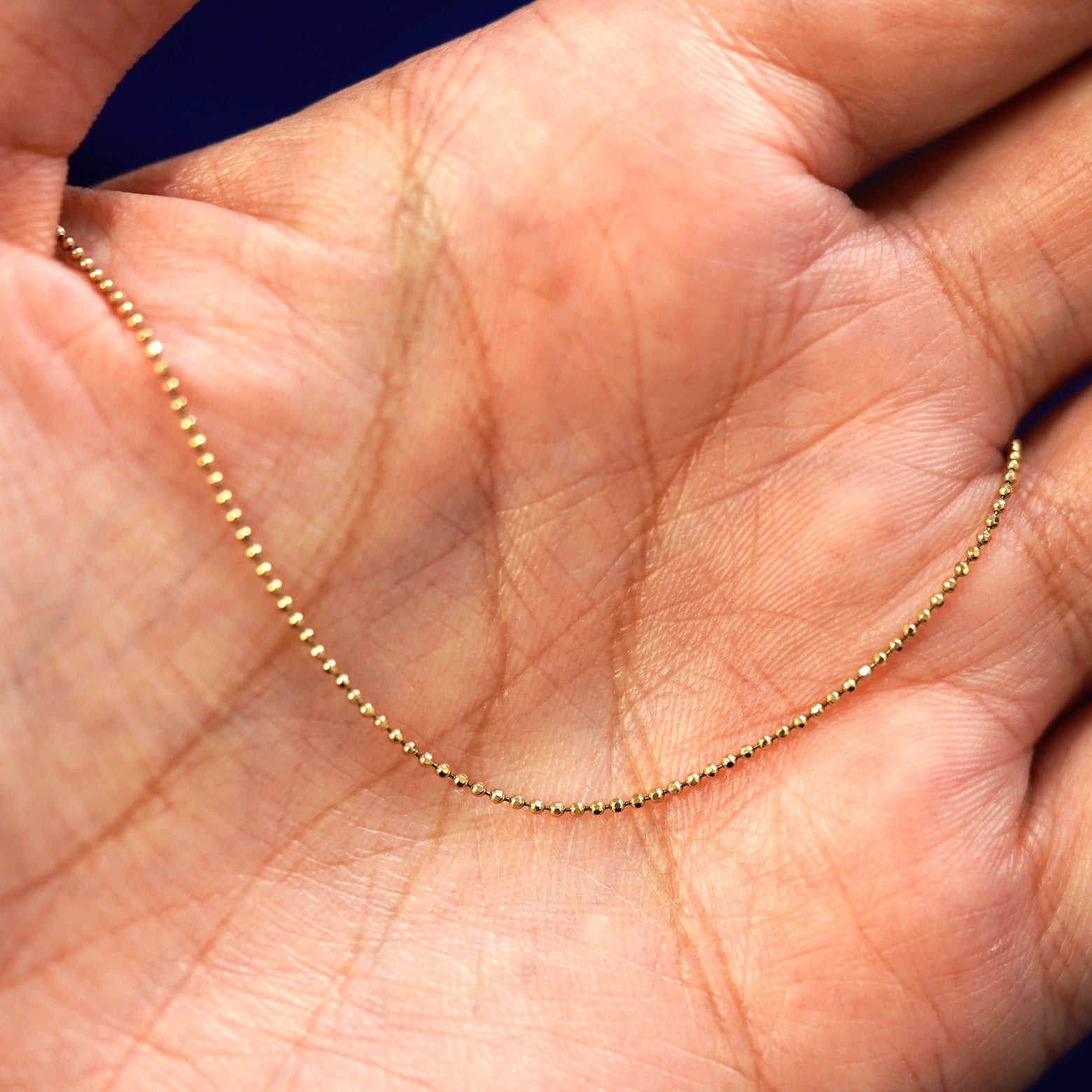 A yellow gold Bead Necklace draped on a model's palm