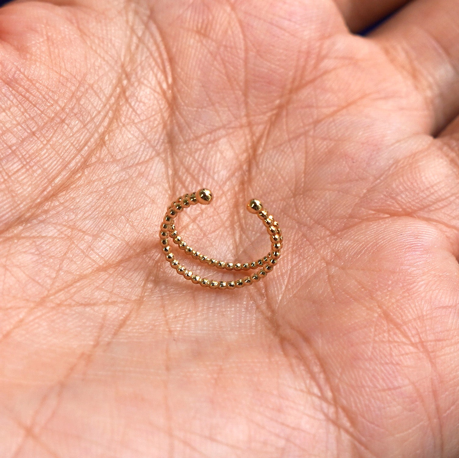 A solid yellow gold Beaded Cuff earring standing upright in a model's palm