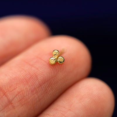 A yellow gold Ball Trio Earring laying facedown on a model's fingers to show the underside view