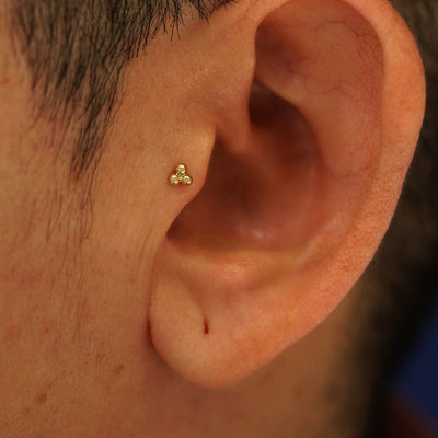 Close up view of a model's ear wearing a 14k yellow gold Ball Trio Flatback as a tragus piercing