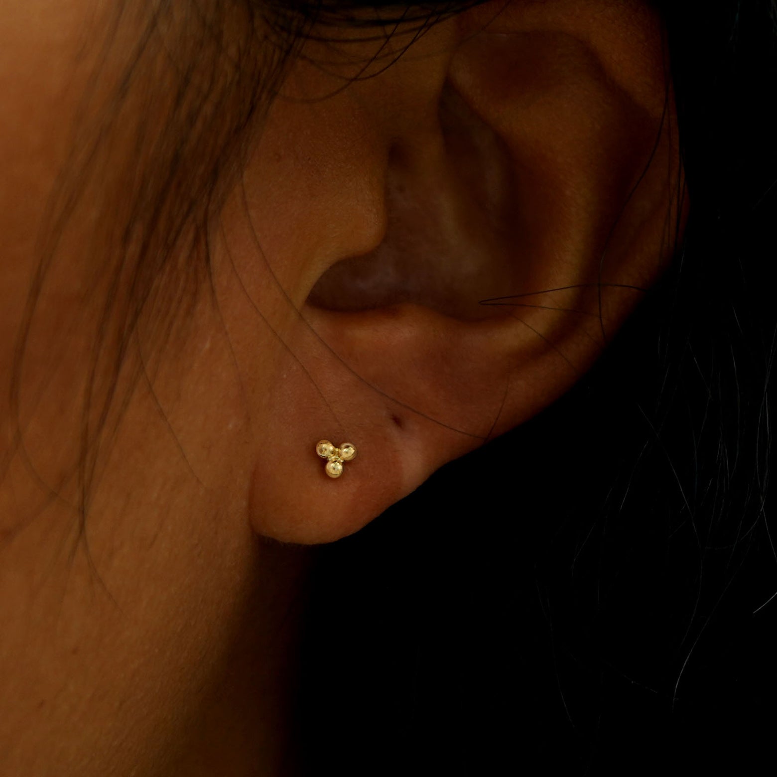 A model's ear wearing a solid yellow gold Ball Trio Flatback Piercing