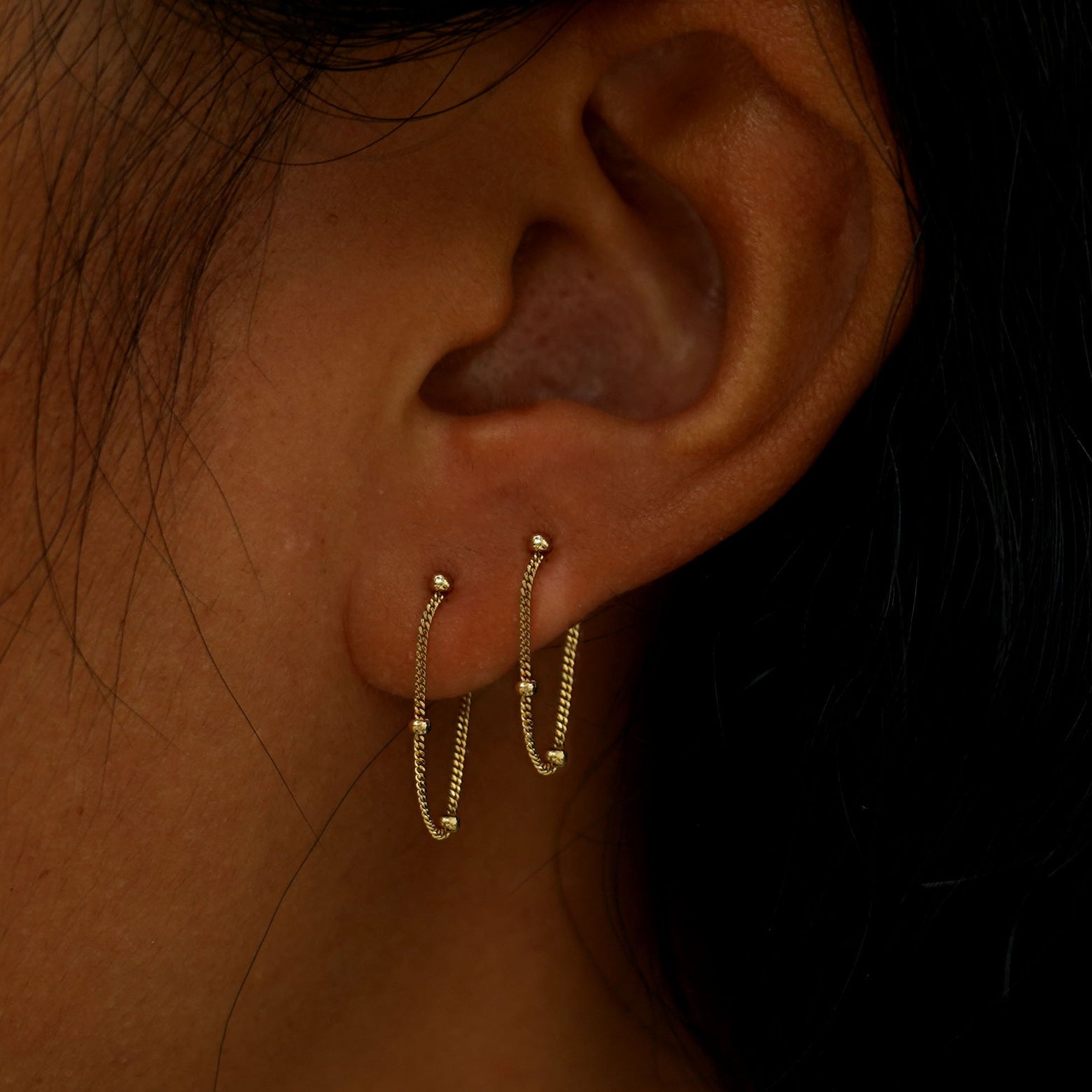 A model's ear wearing two 14k gold Beaded Chain Loop Earrings in two lobe piercings