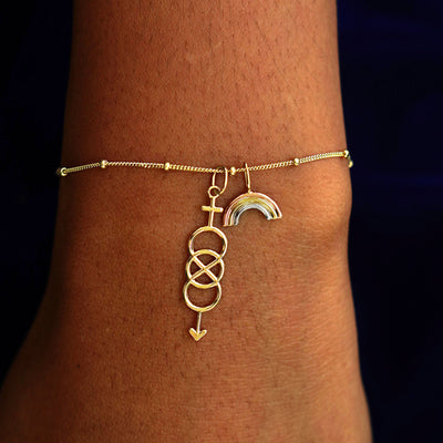 A model's wrist wearing a yellow gold Beaded Essential Chain with a Bisexual Charm and a Rainbow Charm