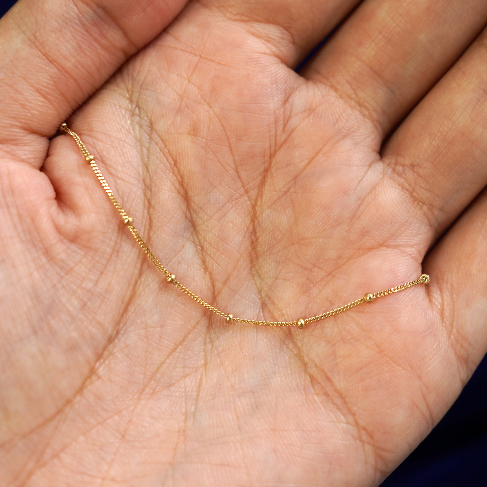 A yellow gold Beaded Essential Lariat Necklace draped on a model's palm to show the chain detials