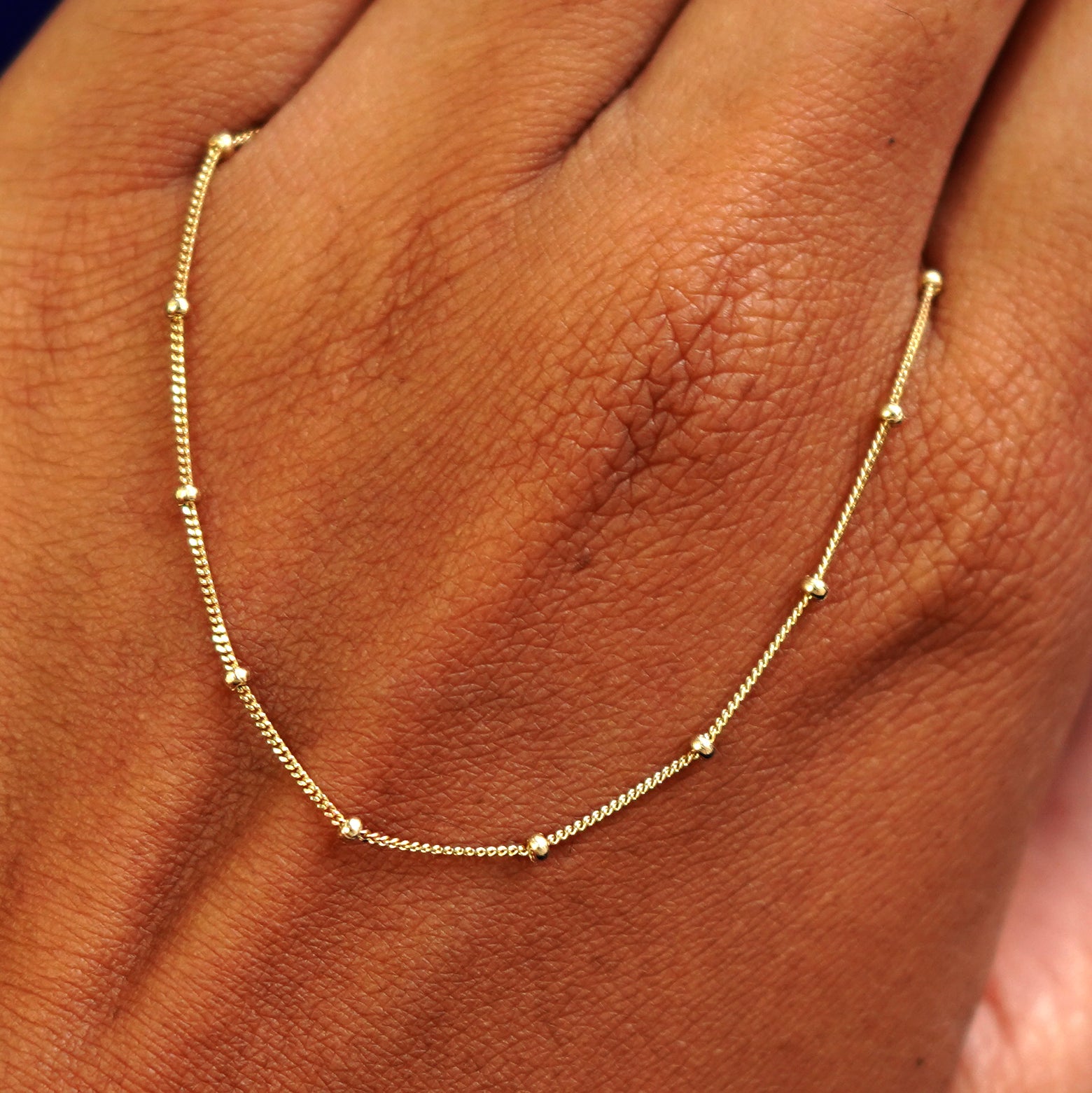 A solid gold Beaded Essential Lariat Necklace resting on the back of a model's hand