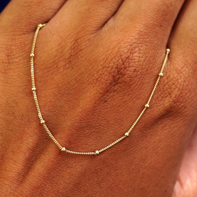 A solid gold Beaded Essential Lariat Necklace resting on the back of a model's hand