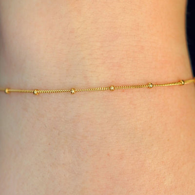 Close up view of a model's wrist wearing a 14k solid gold Beaded Essential Bracelet