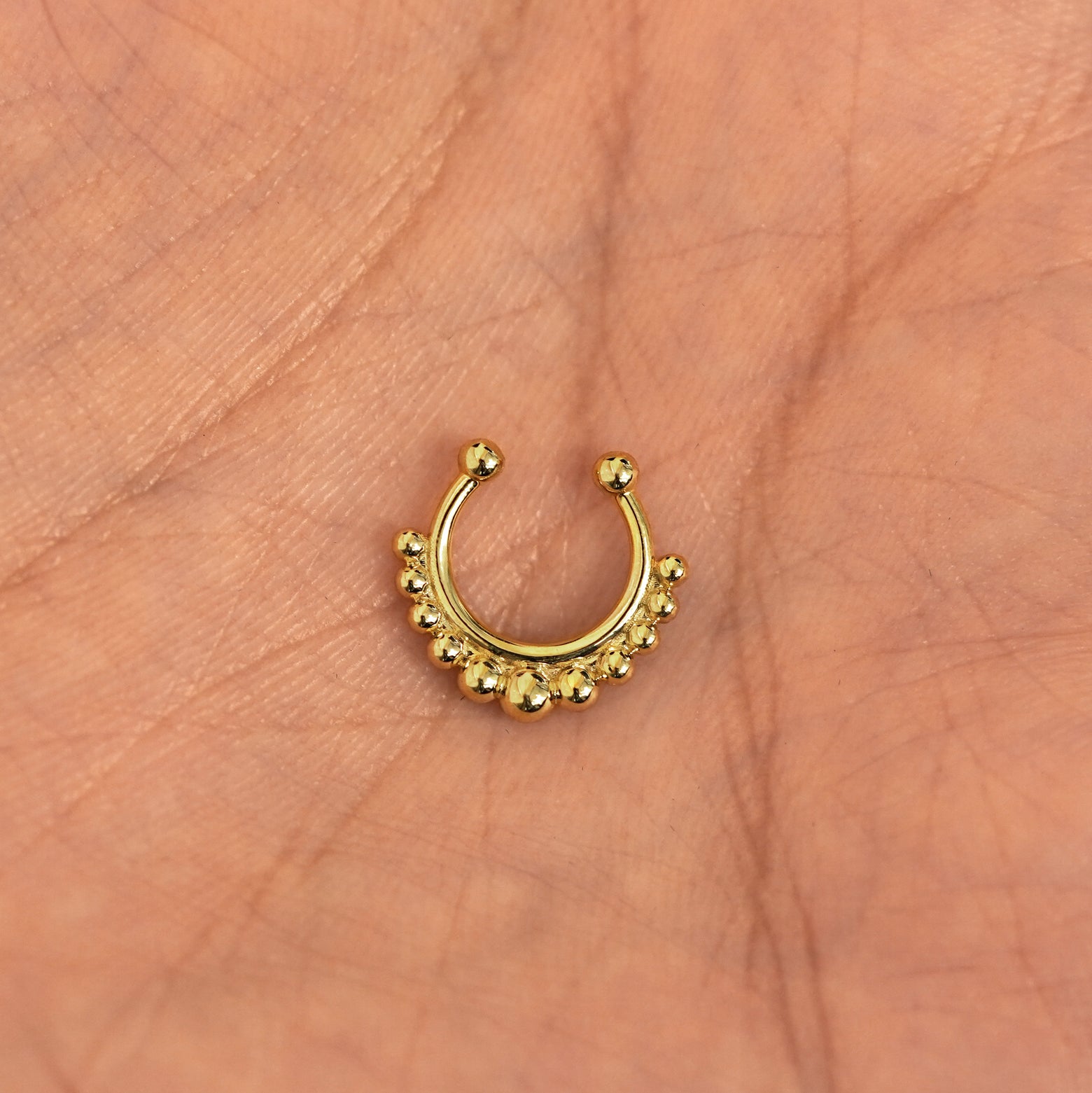 A model's hand holding a 14 karat yellow gold Non-Pierced Beaded Septum