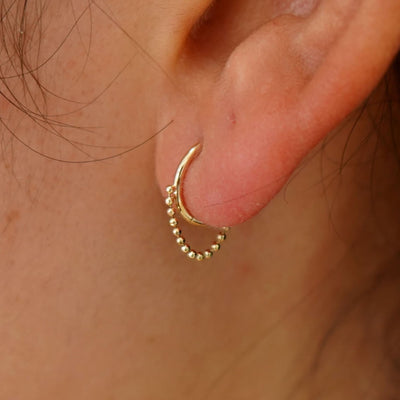 Close up view of a model's ear wearing a yellow gold Beaded Huggie Hoop Earring