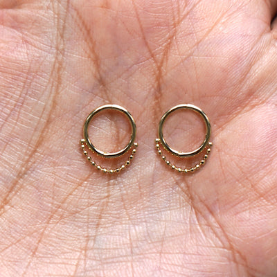 A pair of 14 karat solid gold Beaded Huggie Hoops / Piercings in a model's palm