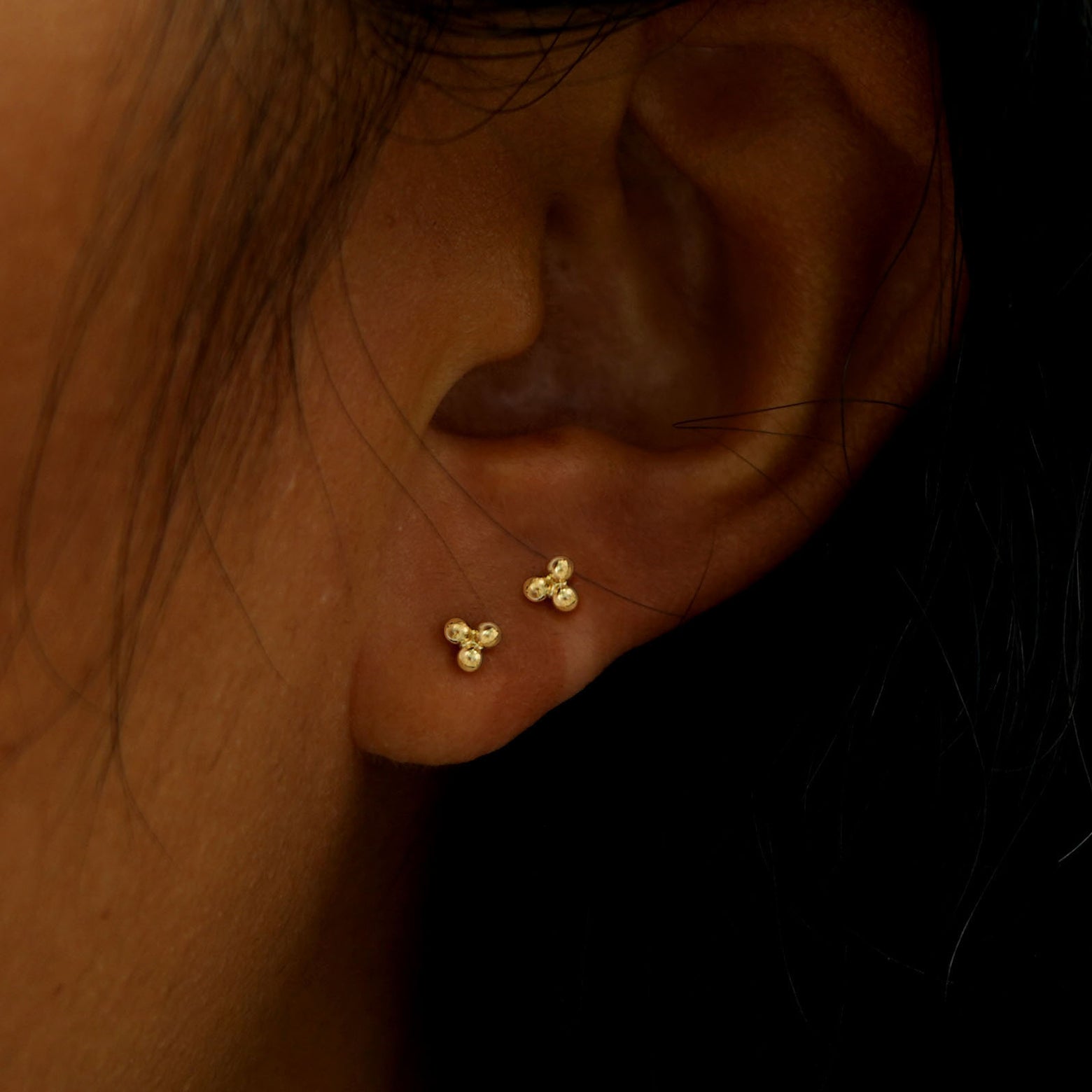 A model's ear wearing two 14k gold Ball Trio Flatback Piercings in two lobe piercings